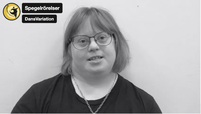 Person med axellångt hår och svart tröja sitter mot en ljus vägg. Texten 'Spegelrörelser' och 'DansVariation' syns i hörnet.