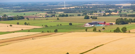 Landskapsvy över åkrar och bondgårdar med röda hus och lador på den svenska landsbygden.