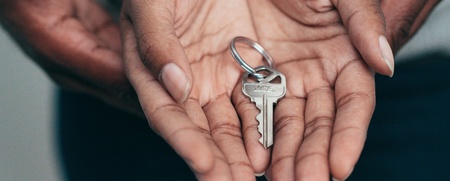 Två händer håller tillsammans en nyckel på en nyckelring, fokus på händer och nyckel.