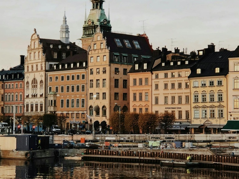 Stadshus och kyrktorn speglas i vattnet vid en kaj i en europeisk stad, troligen Stockholm.