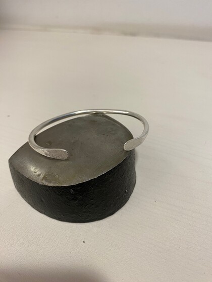 En enkel silverfärgad armring ligger på ett halvt klotformat metallblock på ett vitt underlag.