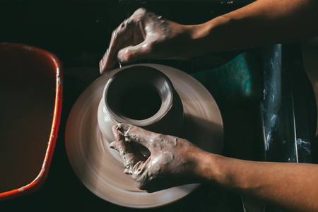 Händer formar en lerkruka på en drejskiva i ett keramikverkstad.