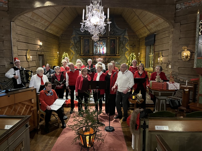 En kör sjunger i en träkyrka dekorerad för jul, med musiker och publik närvarande.