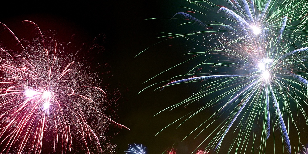 Färgglada fyrverkerier lyser upp natthimlen över ett bostadsområde med flerfamiljshus.