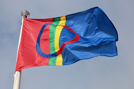 Samiska flaggan vajar mot en blå himmel. Flaggan har rött, blått, grönt och gult med en cirkel i mitten.