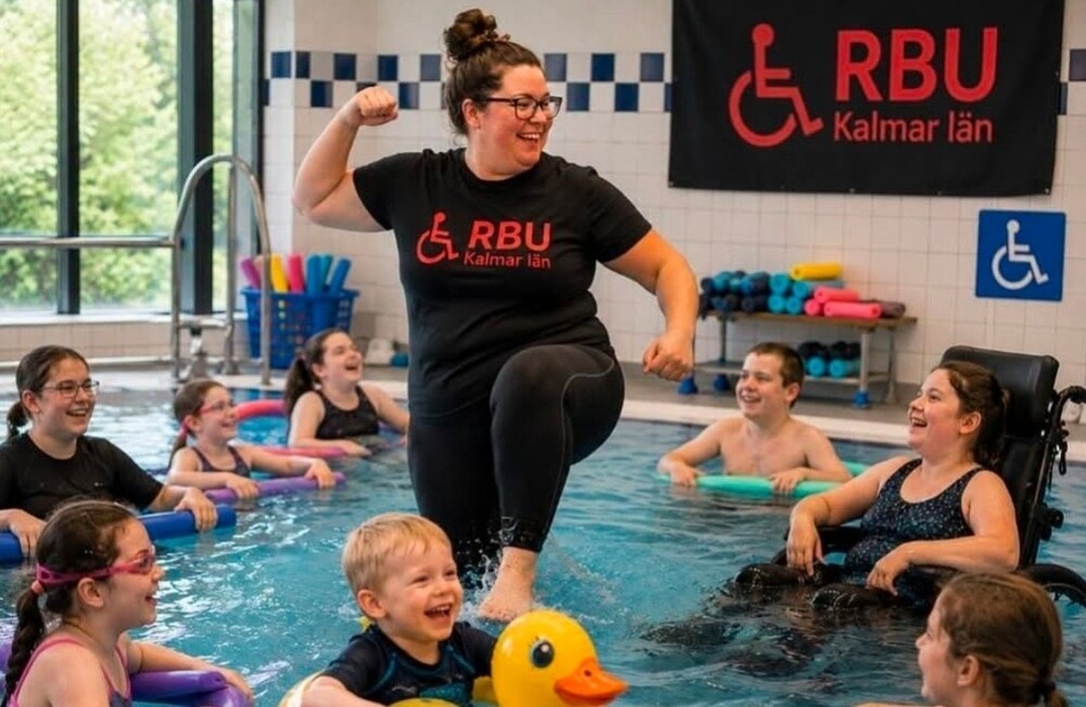 En grupp barn och vuxna har roligt i en simhall, ledaren står i vattnet och visar styrka.