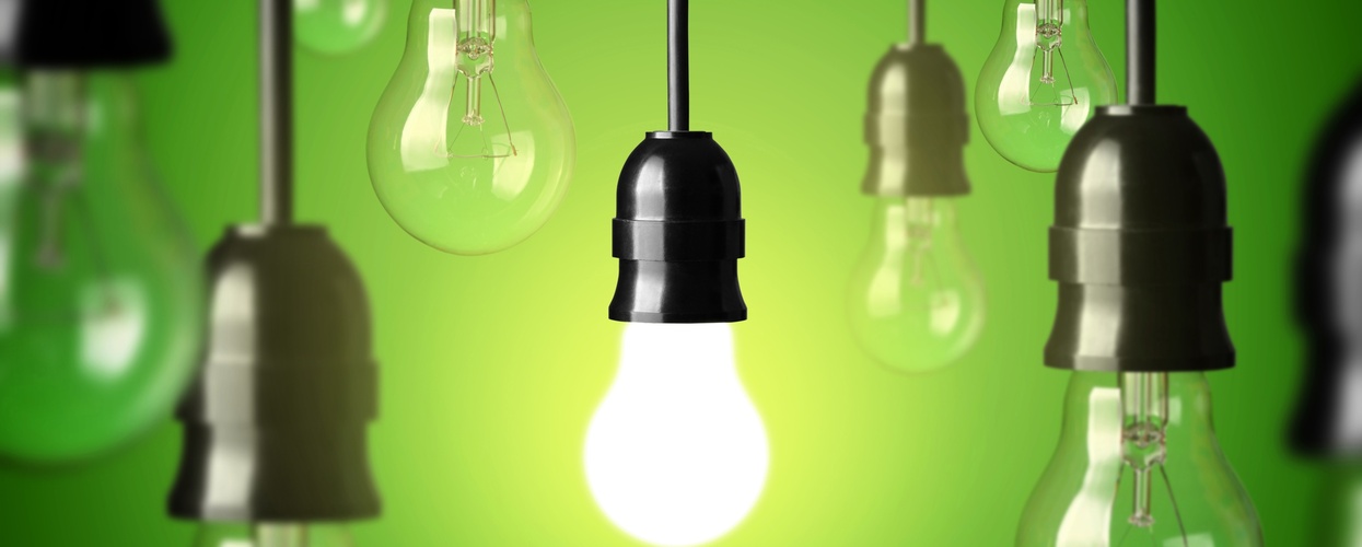 Flera hängande glödlampor mot grön bakgrund, en lampa lyser medan resten är släckta.