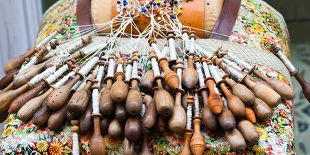 Närbild av en spetskudde med många träspolar och pågående knypplingsarbete.