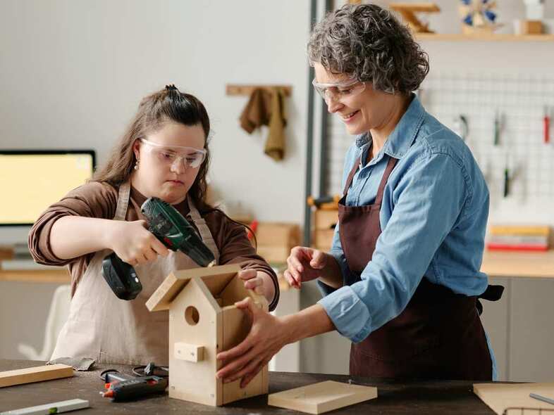 En slöjdlärare hjälper en elev att montera ihop en fågelholk.