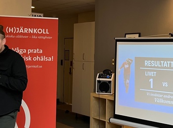 Person håller mikrofon och står framför rollups och en projektorduk med resultat på svenska.