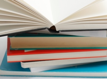 En hög med böcker där den översta boken är uppslagen och resten är stängda, mot vit bakgrund.