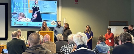 Möte eller presentation i konferensrum med flera personer, en talare vid podiet och publik som lyssnar.