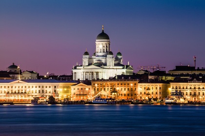 Upplyst domkyrka och byggnader vid vattnet i Helsingfors under skymning.