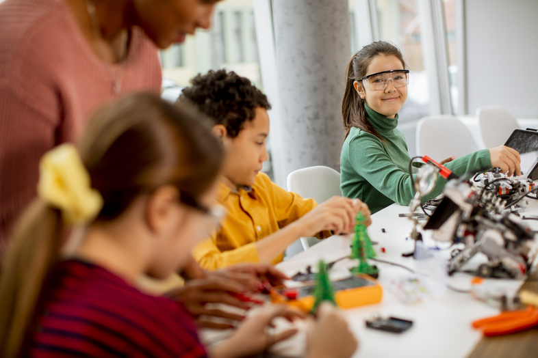Barn bygger och experimenterar med robotik och elektronik vid ett bord tillsammans med en vuxen.