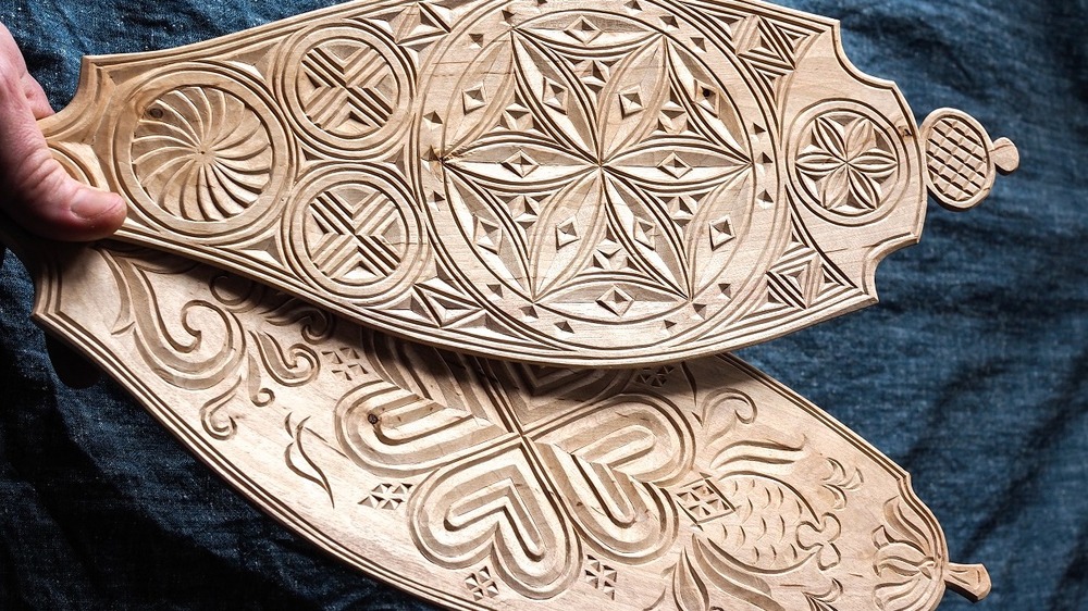 Två träföremål med intrikata sniderier och geometriska mönster hålls i en hand.