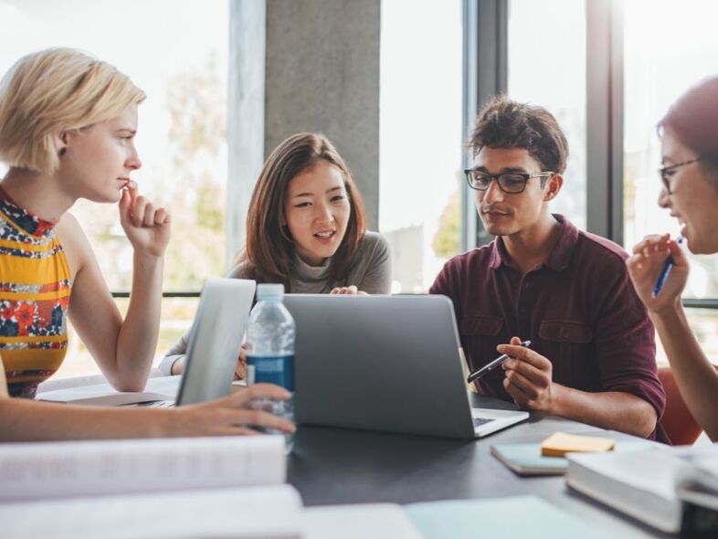 Fyra unga personer sitter samlade kring en laptop.