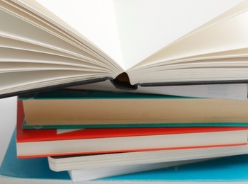 En hög med böcker där den översta boken är uppslagen och resten är stängda, mot vit bakgrund.