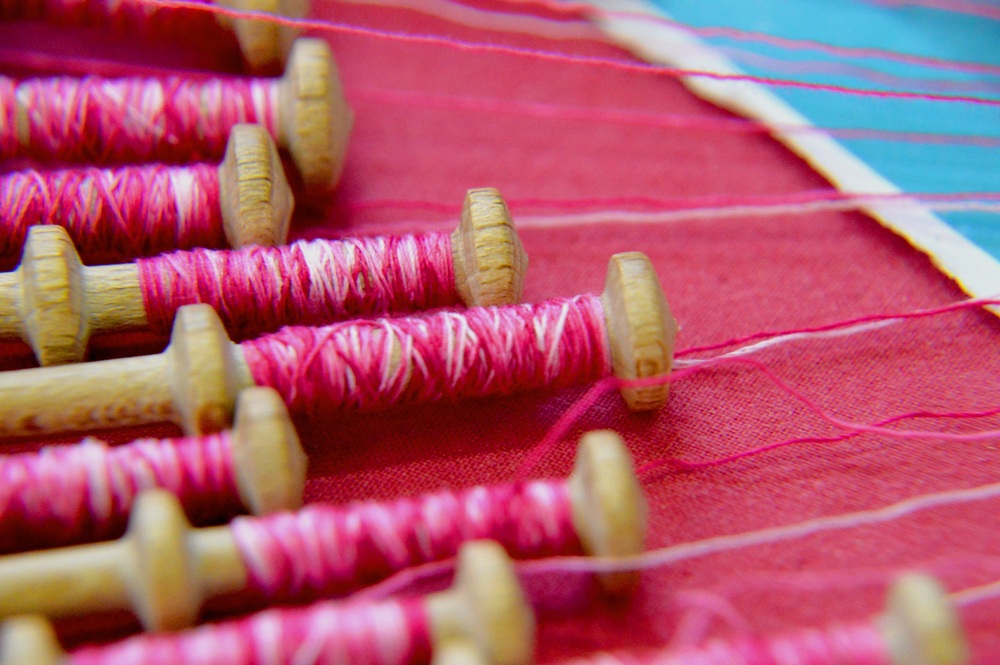 Närbild av flera trådrullar med rosa tråd på ett rött tygstycke.