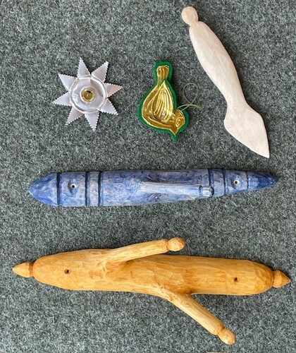 Fem handgjorda träföremål och en fågelprydnad ligger på en grå filt.
