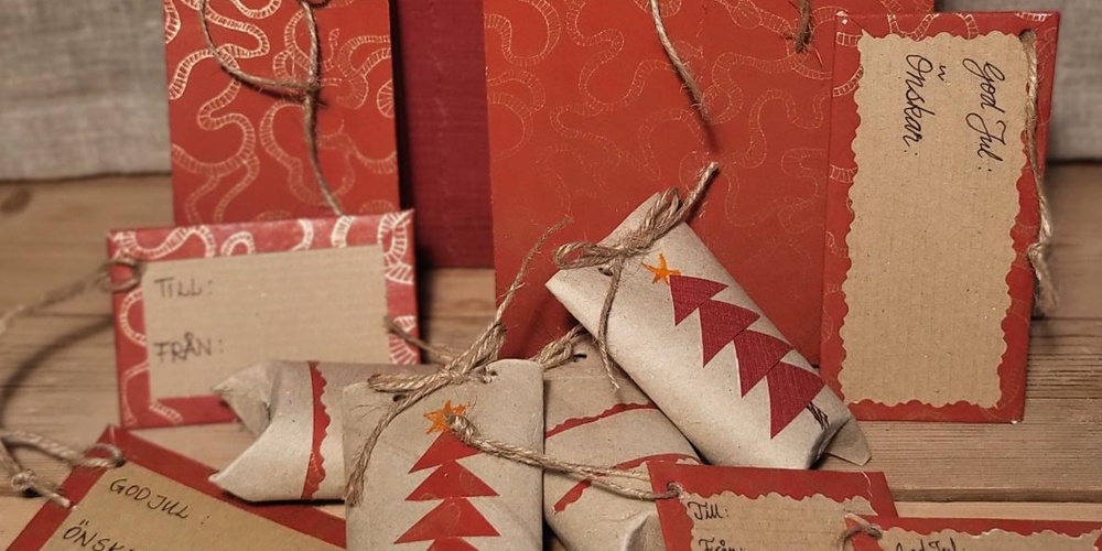 Handgjorda julklappsetiketter och presentförpackningar i rött och brunt med snören på ett träbord.