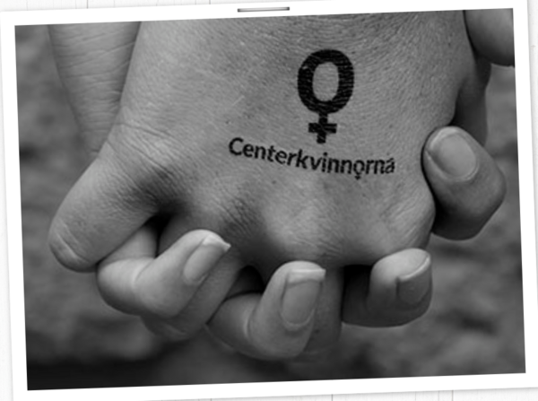 En svart och vit bild på två händer som håller hand. På ena handen är det tatuerat logotypen för centerkvinnorna.