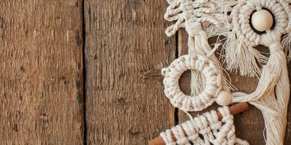 Makramé juldekorationer hänger på en rustik trävägg, inklusive gran, krans och geometriska former.