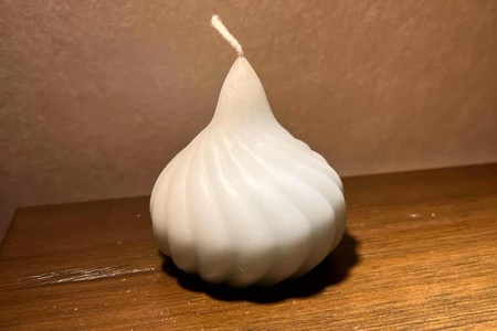 En vit, rund och räfflad ljuslykta i form av en lök står på ett träbord mot en beige bakgrund.