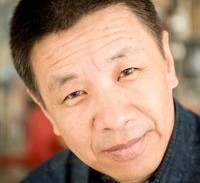 Person med kort mörkt hår och blå skjorta står framför en suddig bakgrund med böcker.