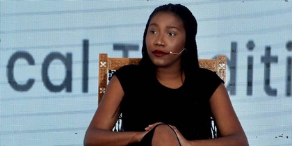 Person sitter på en stol med armarna vilande och benen i kors framför en stor textskärm.