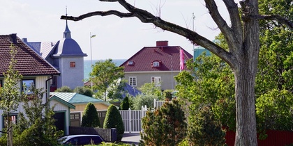 Vy över ett bostadsområde med färgglada hus, trädgårdar och ett stort träd i förgrunden.