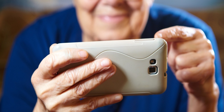 En äldre person håller en smartphone med båda händer och tittar på skärmen.