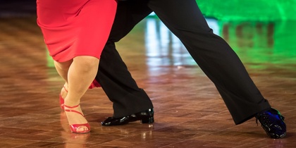 Två personer dansar tillsammans på ett dansgolv, endast deras ben och fötter syns.