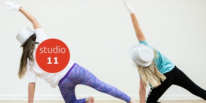 Två personer dansar i studio, bär hattar och handskar, sträcker armarna uppåt mot väggen.