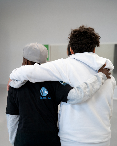 Två personer står med armarna om varandra, sedda bakifrån, i en ljus inomhusmiljö.