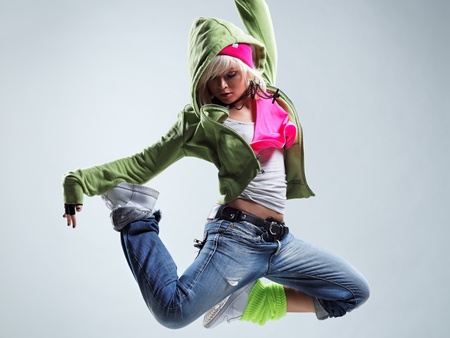 En ung kvinna i färgglada kläder hoppar i luften i en dynamisk danspose mot en ljus bakgrund.