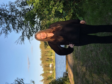 Person i svart klädsel står utomhus vid en sjö med skog i bakgrunden, ansiktet är suddat.