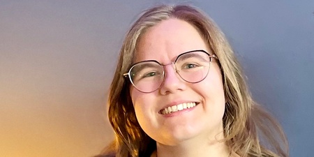 Två leende personer sitter tillsammans i en blå soffa i ett rum med blå vägg och grön växt.