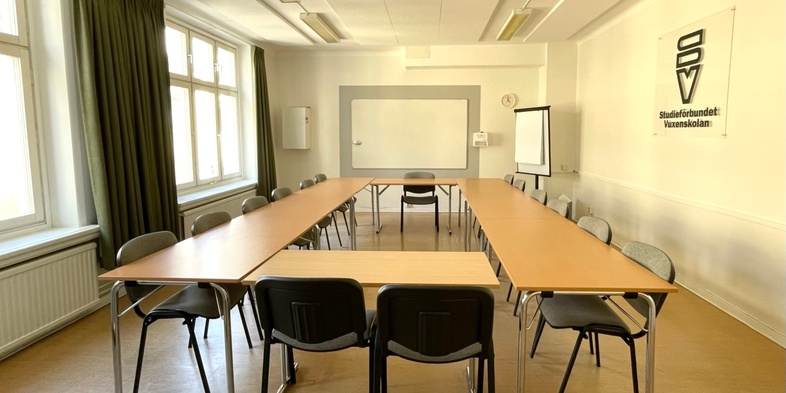 Ett ljust konferensrum med U-formade bord, svarta stolar, stora fönster och en whiteboard.