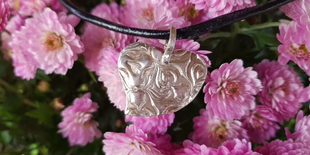 Silverhjärthalsband med blommönster hänger framför rosa krysantemumblommor.