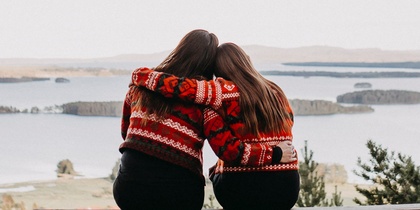 Två personer sitter på en bänk med ryggen mot kameran och ser ut över en sjö och öar i ett skogslandskap.