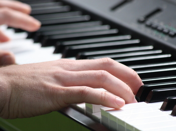 Närbild på händer som spelar på ett svartvitt piano eller keyboard.