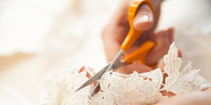 Närbild av händer som klipper vit spets med en sax.