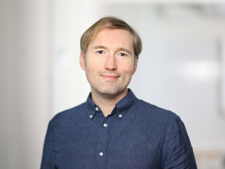 Person i blå skjorta står inomhus mot en ljus, suddig bakgrund.