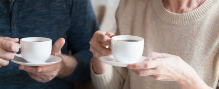 Två personer håller vita kaffekoppar och pratar, endast överkroppar och händer syns.