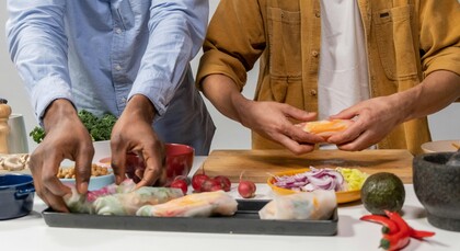 Två personer förbereder färska vårrullar med grönsaker på ett köksbord.