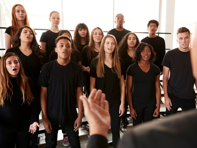 En grupp ungdomar sjunger i kör, ledda av en dirigent i ett ljust rum.