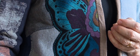 Närbild av en person som bär en färgglad jacka med fjärilsmotiv och håller i kragen.