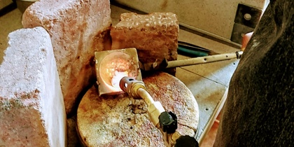En arbetsstation för smyckestillverkning med gasbrännare, tegelstenar och smält metall.