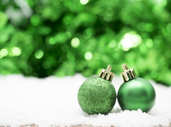 Två gröna julgranskulor står på konstsnö med suddig grön bakgrund.
