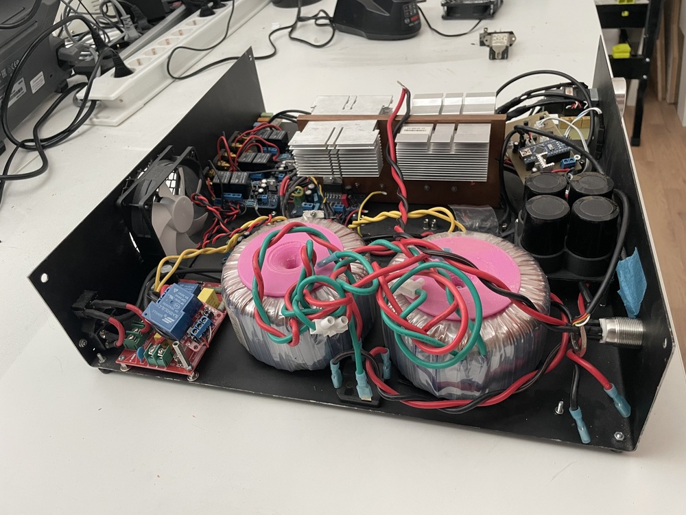 Elektronisk apparatlåda med transformatorer, kylflänsar, fläkt och kretskort på ett arbetsbord.